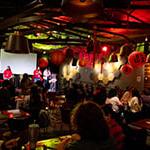 一群人聚集在满帆的树屋，客人们坐下来，主持人在舞台上. 房间里灯光昏暗，装饰着农历新年的红纸灯笼.