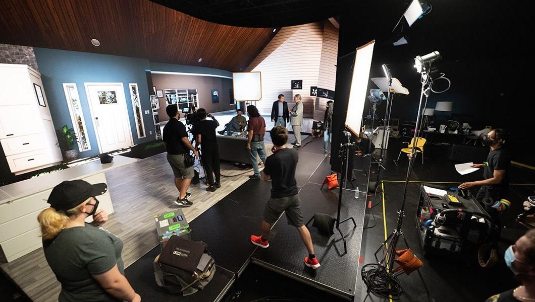 Crew members set up 相机 和 make adjustments to a virtual living room backdrop between scenes.